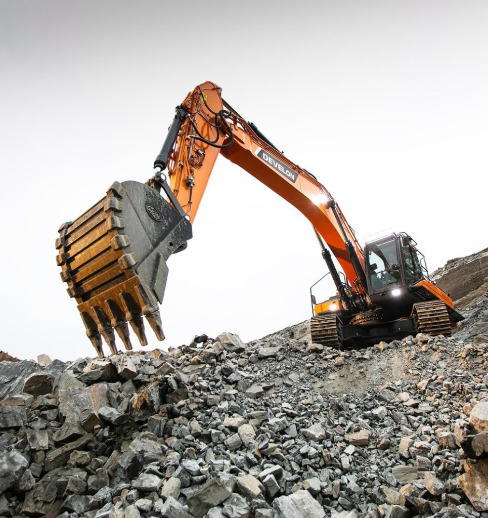 A Develon excavator breaking through a pile of rocks, showcasing its strength and efficiency in heavy-duty earth-moving equipment tasks