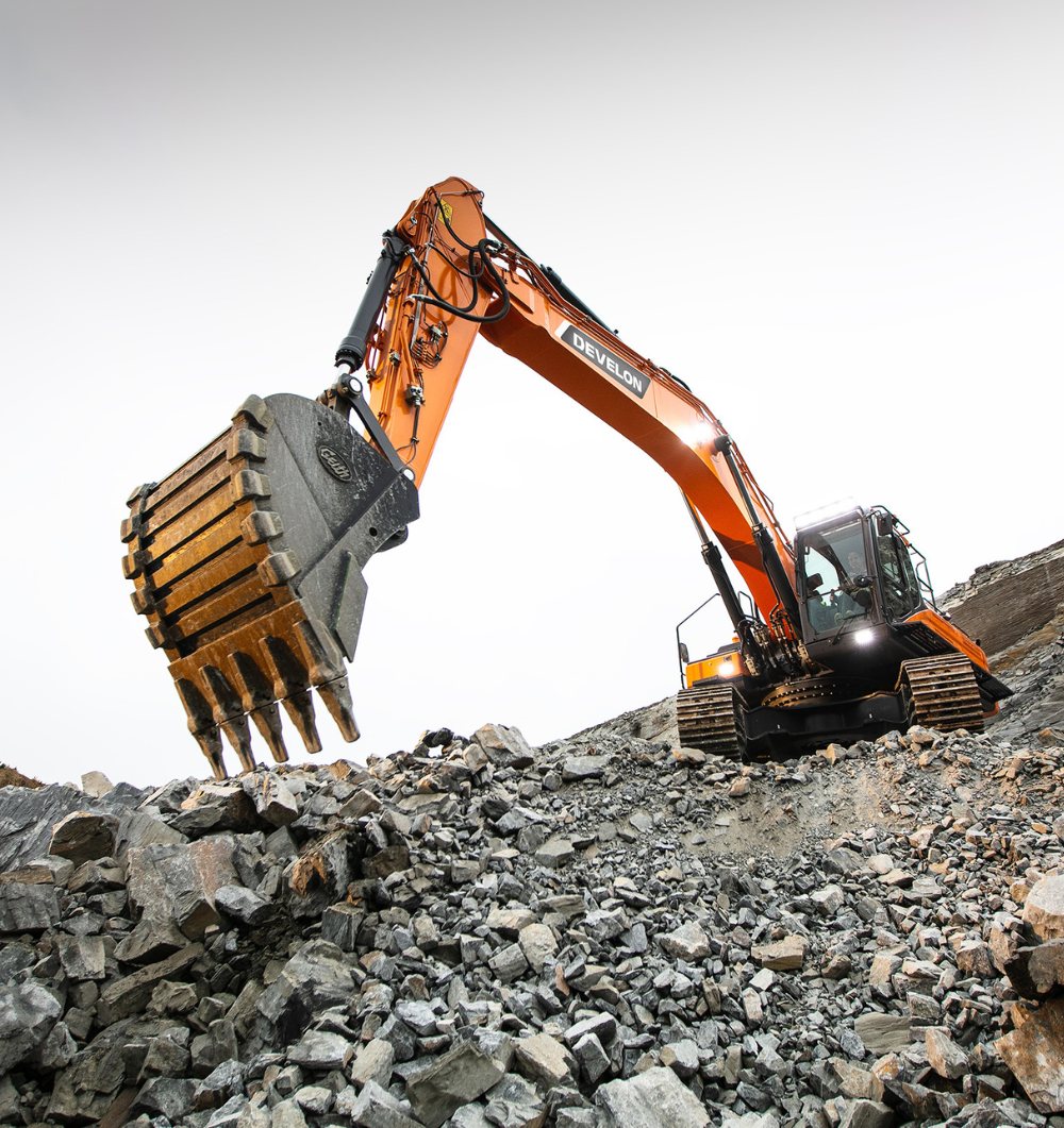 A Develon excavator breaking through a pile of rocks, showcasing its strength and efficiency in heavy-duty earth-moving equipment tasks