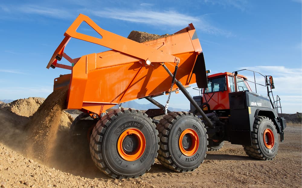 A Develon articulated dump truck unloading soil on a construction site, showcasing its stability, durability, and efficiency in tough conditions