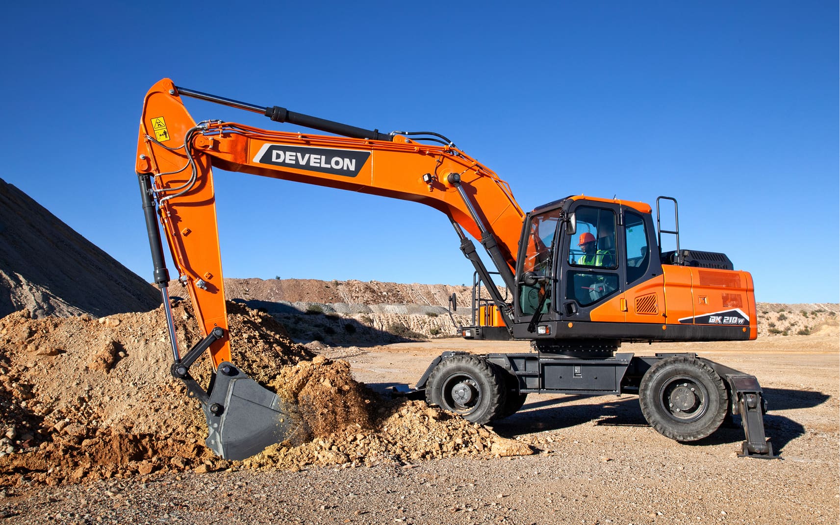 Excavation construction with Develon excavator showcasing fuel efficiency and force, digging a massive hole in a forest setting